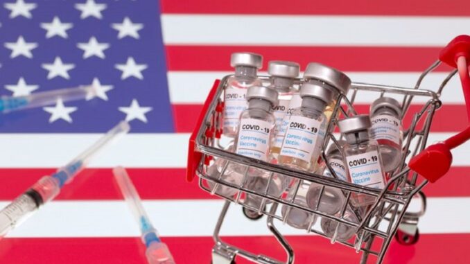 FILE PHOTO: A small shopping basket filled with vials labeled "COVID-19 - Coronavirus Vaccine" and medical syringes are placed on a U.S. flag