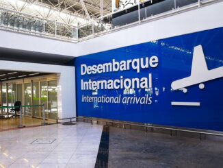 A imagem mostra um painel azul em uma parede de aeroporto. Nele é possível esta escrito "Desembarque Internacional/International Arrivals" e com a silhueta branca de um avião ao lado.