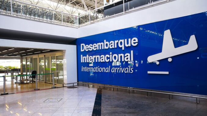 A imagem mostra um painel azul em uma parede de aeroporto. Nele é possível esta escrito "Desembarque Internacional/International Arrivals" e com a silhueta branca de um avião ao lado.
